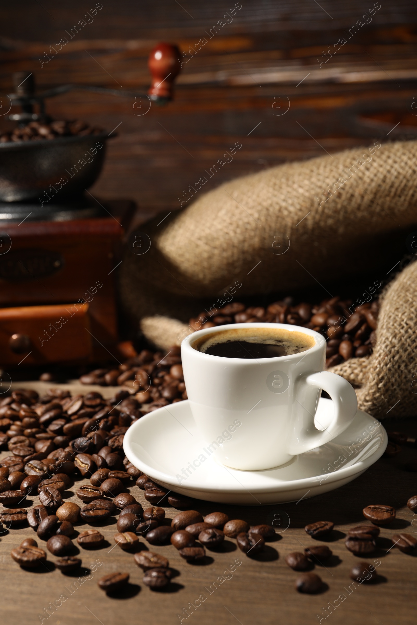Photo of Aromatic coffee in cup, beans and grinder on wooden table
