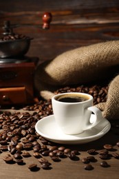 Photo of Aromatic coffee in cup, beans and grinder on wooden table