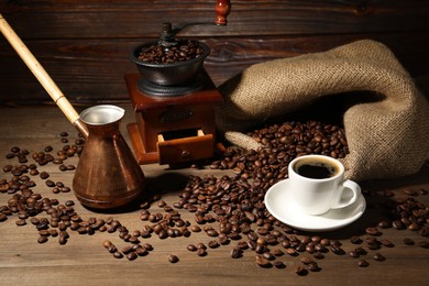 Photo of Aromatic coffee in cup, beans, cezve and grinder on wooden table