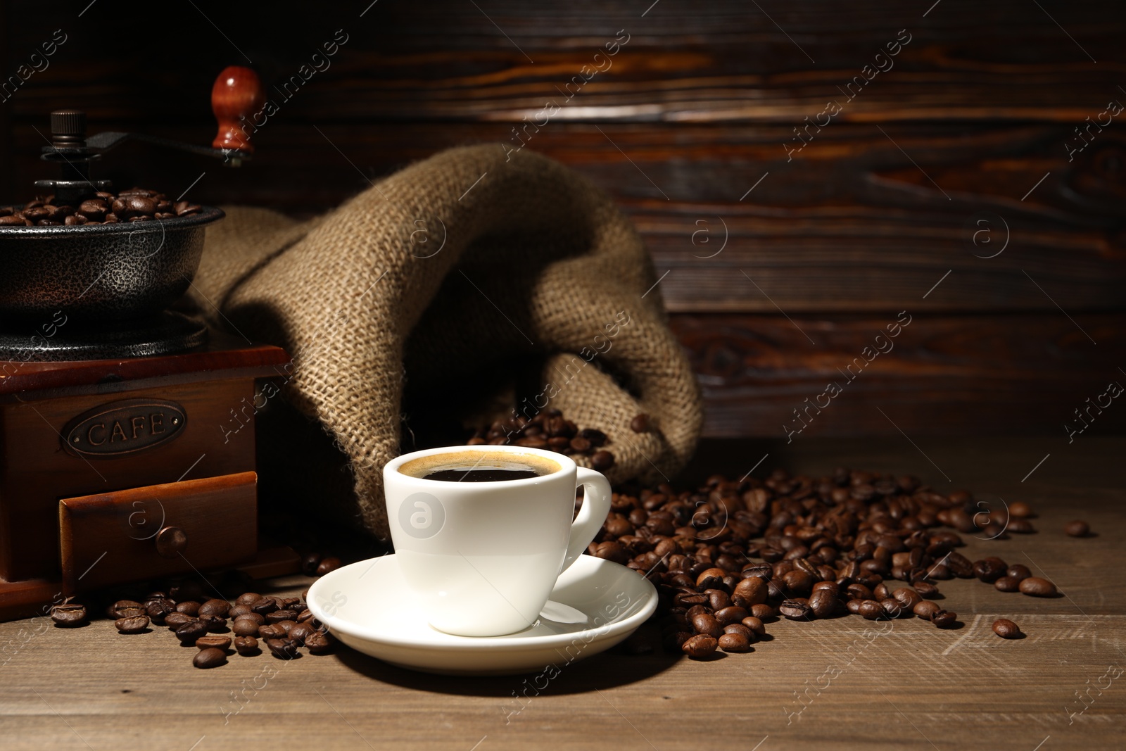 Photo of Aromatic coffee in cup, beans and grinder on wooden table, space for text