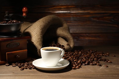 Photo of Aromatic coffee in cup, beans and grinder on wooden table, space for text