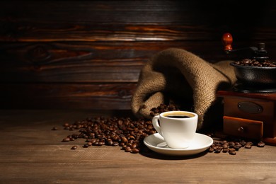 Photo of Aromatic coffee in cup, beans and grinder on wooden table, space for text