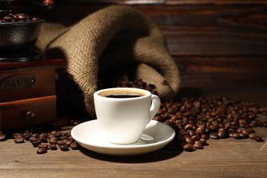 Photo of Aromatic coffee in cup, beans and grinder on wooden table