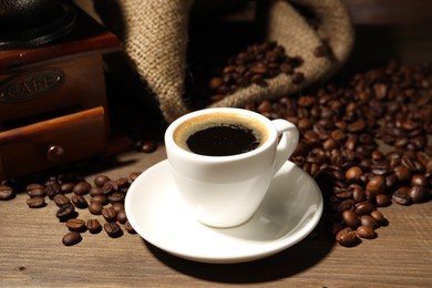 Photo of Aromatic coffee in cup, beans and grinder on wooden table, closeup
