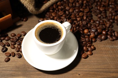 Photo of Aromatic coffee in cup and beans on wooden table, closeup
