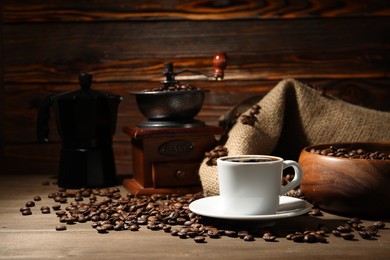 Photo of Aromatic coffee in cup, beans, moka pot and grinder on wooden table