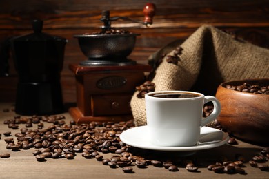 Photo of Aromatic coffee in cup, beans, moka pot and grinder on wooden table, closeup