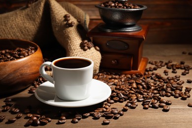 Photo of Aromatic coffee in cup, beans and grinder on wooden table