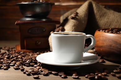 Photo of Aromatic coffee in cup, beans and grinder on wooden table, closeup