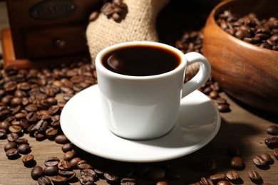 Photo of Aromatic coffee in cup and beans on wooden table, closeup