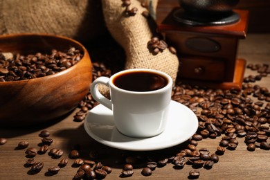 Photo of Aromatic coffee in cup, beans and grinder on wooden table, closeup