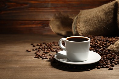 Photo of Aromatic coffee in cup and beans on wooden table, space for text