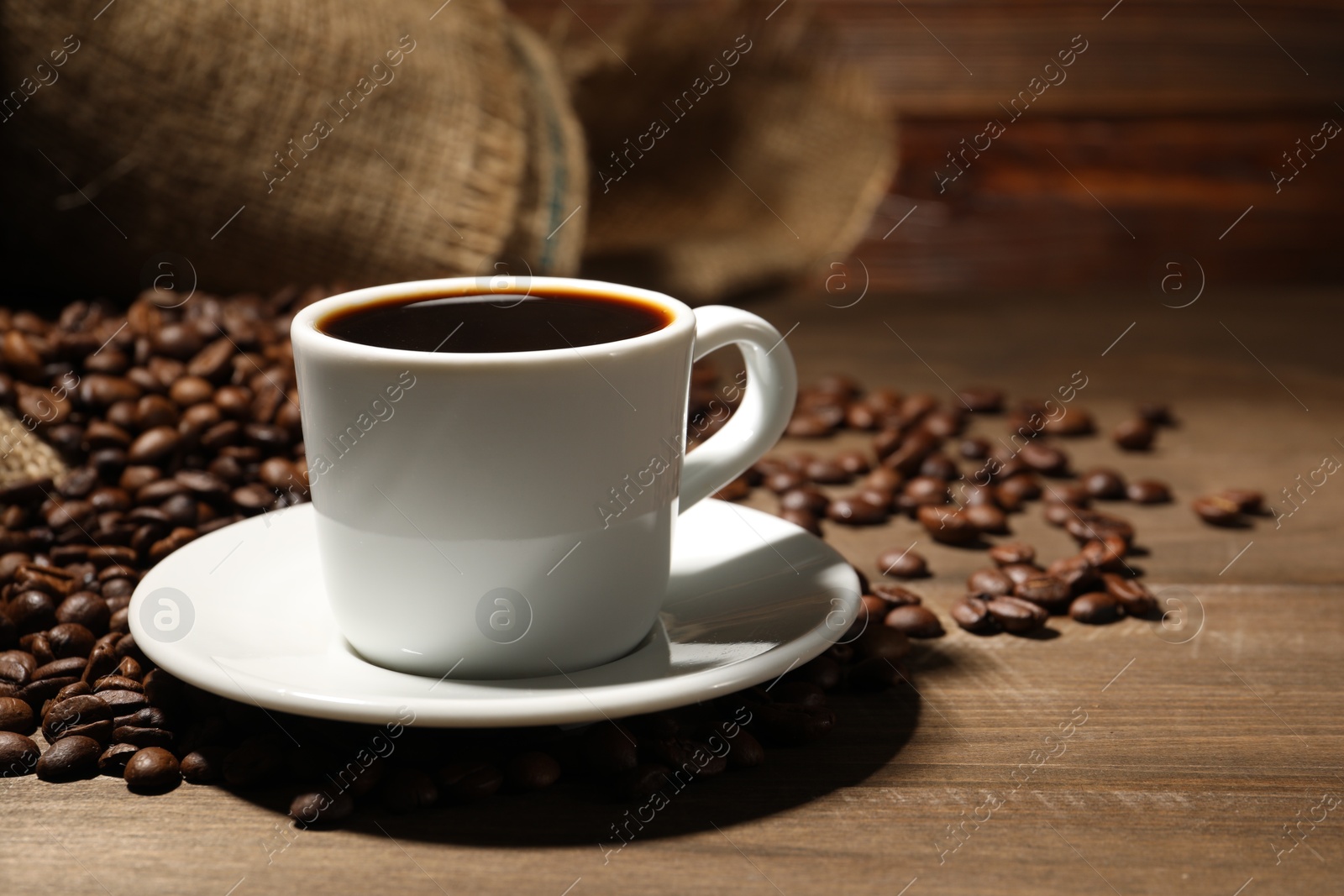 Photo of Aromatic coffee in cup and beans on wooden table, closeup. Space for text