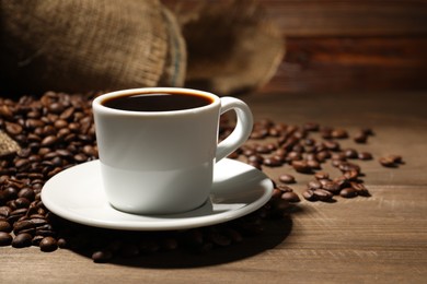 Photo of Aromatic coffee in cup and beans on wooden table, closeup. Space for text