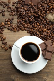 Photo of Aromatic coffee in cup, beans and pieces of chocolate on wooden table, flat lay