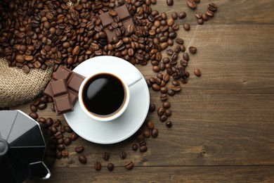 Photo of Aromatic coffee in cup, beans, chocolate and moka pot on wooden table, flat lay. Space for text