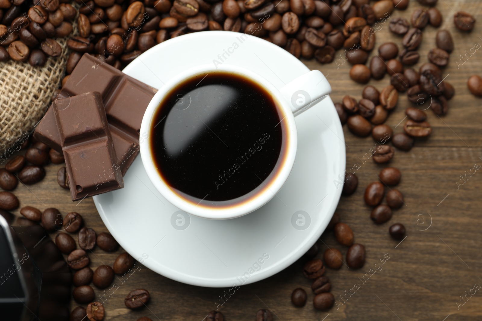 Photo of Aromatic coffee in cup, beans and pieces of chocolate on wooden table, flat lay