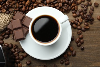 Photo of Aromatic coffee in cup, beans and pieces of chocolate on wooden table, flat lay