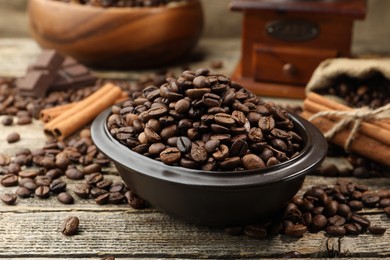 Photo of Aromatic coffee beans in bowl and cinnamon on wooden table, closeup