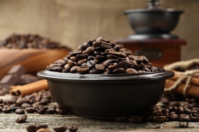Photo of Aromatic coffee beans in bowl and cinnamon on wooden table, closeup