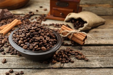 Photo of Aromatic coffee beans in bowl and cinnamon on wooden table, closeup. Space for text