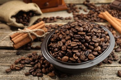 Photo of Aromatic coffee beans in bowl and cinnamon on wooden table, closeup