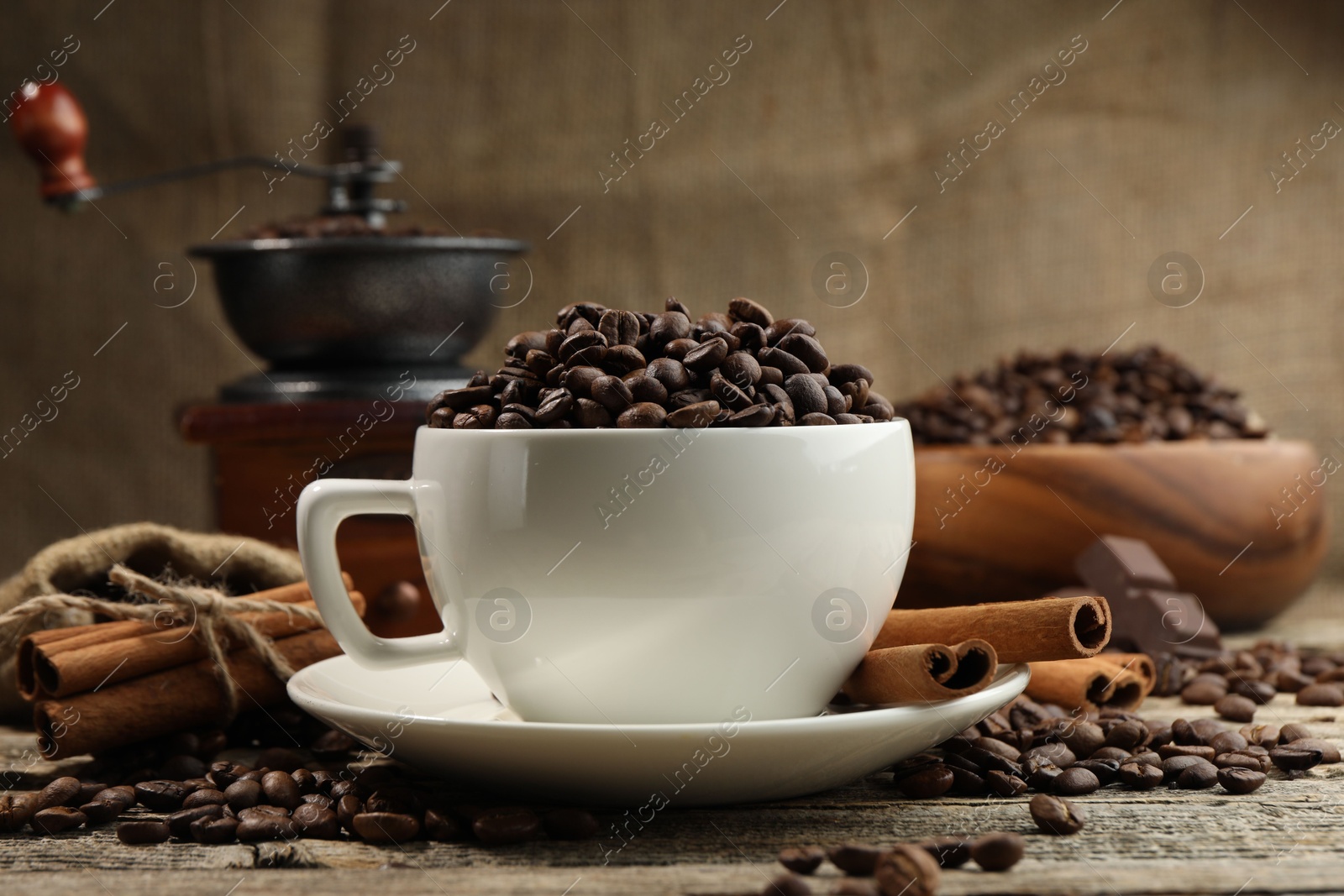Aromatic coffee beans in cup, cinnamon and grinder on wooden table, closeup Photo of Aromatic coffee beans in cup, cinnamon and grinder on wooden table, closeup