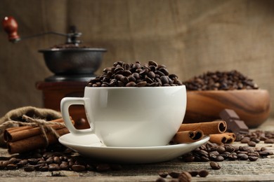 Photo of Aromatic coffee beans in cup, cinnamon and grinder on wooden table, closeup