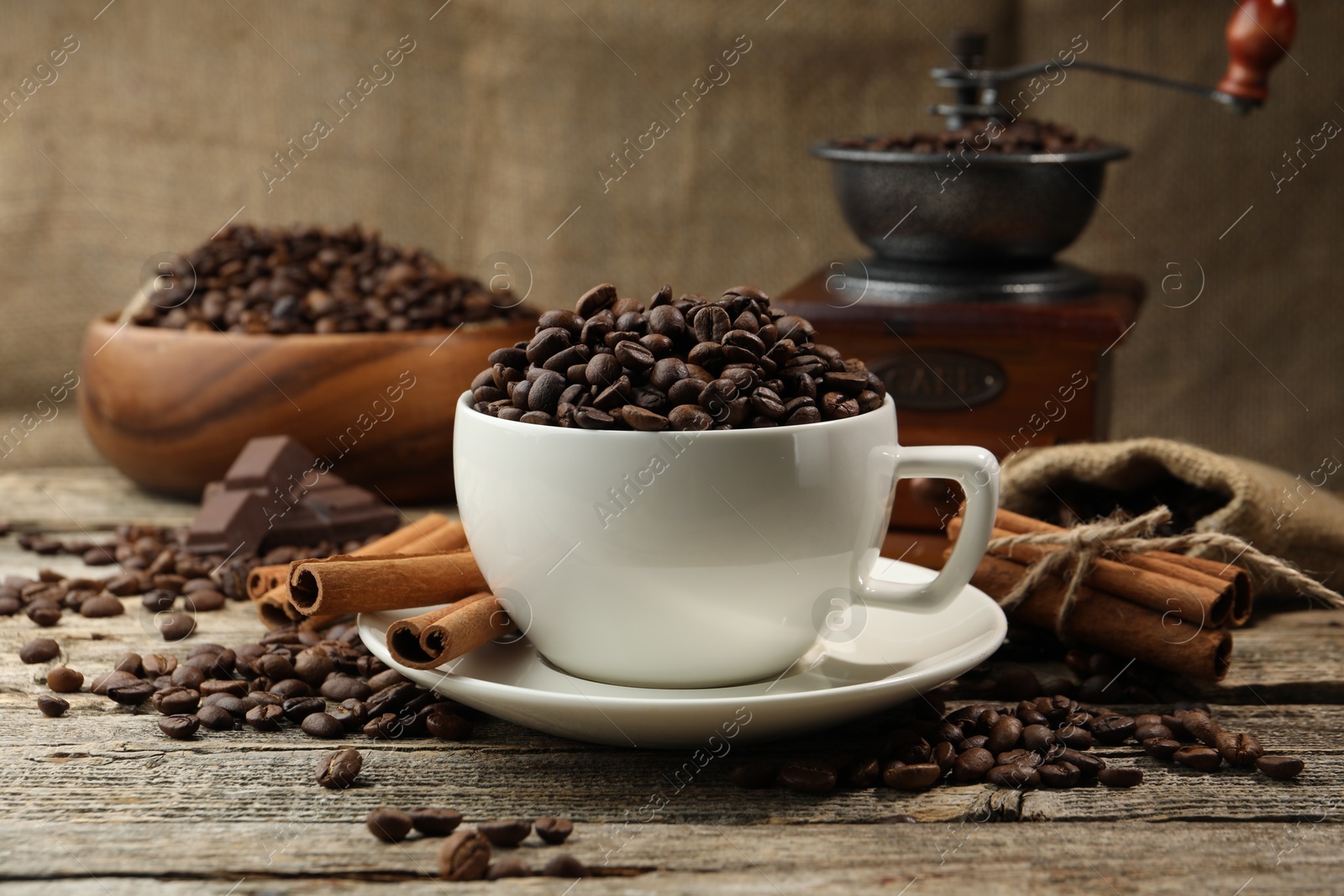 Aromatic coffee beans in cup, cinnamon and grinder on wooden table Photo of Aromatic coffee beans in cup, cinnamon and grinder on wooden table