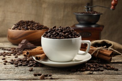 Photo of Aromatic coffee beans in cup, cinnamon and grinder on wooden table