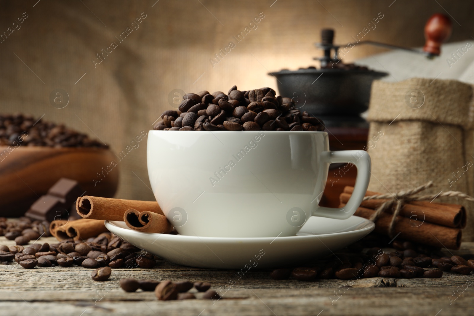 Aromatic coffee beans in cup, cinnamon and grinder on wooden table, closeup Photo of Aromatic coffee beans in cup, cinnamon and grinder on wooden table, closeup