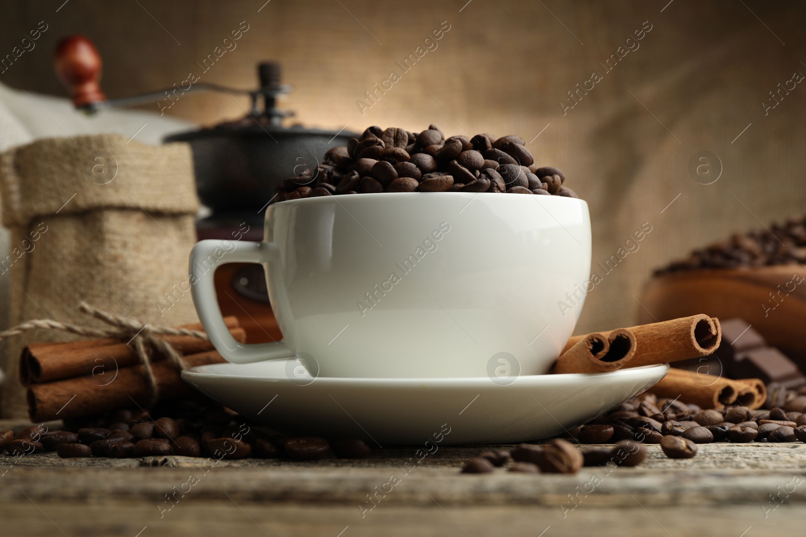Aromatic coffee beans in cup, cinnamon and grinder on wooden table, closeup Photo of Aromatic coffee beans in cup, cinnamon and grinder on wooden table, closeup
