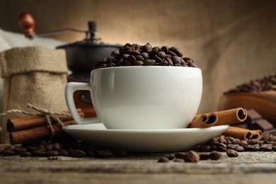 Photo of Aromatic coffee beans in cup, cinnamon and grinder on wooden table, closeup