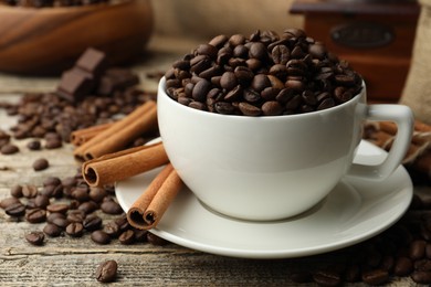 Photo of Aromatic coffee beans in cup, cinnamon and pieces of chocolate on wooden table, closeup