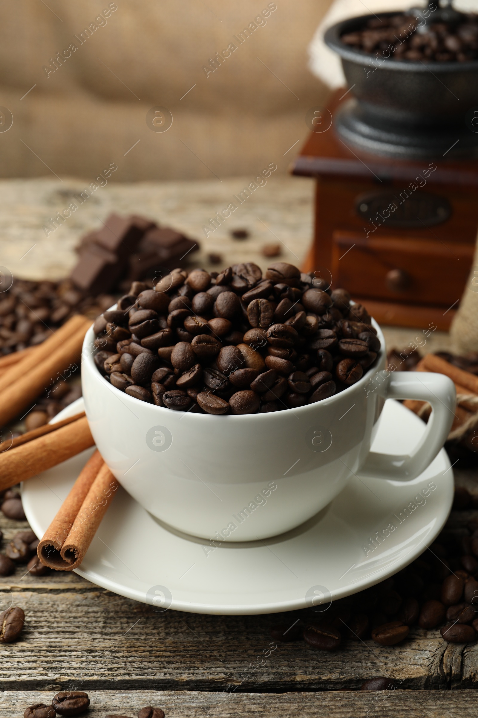 Aromatic coffee beans in cup, cinnamon and grinder on wooden table, closeup Photo of Aromatic coffee beans in cup, cinnamon and grinder on wooden table, closeup