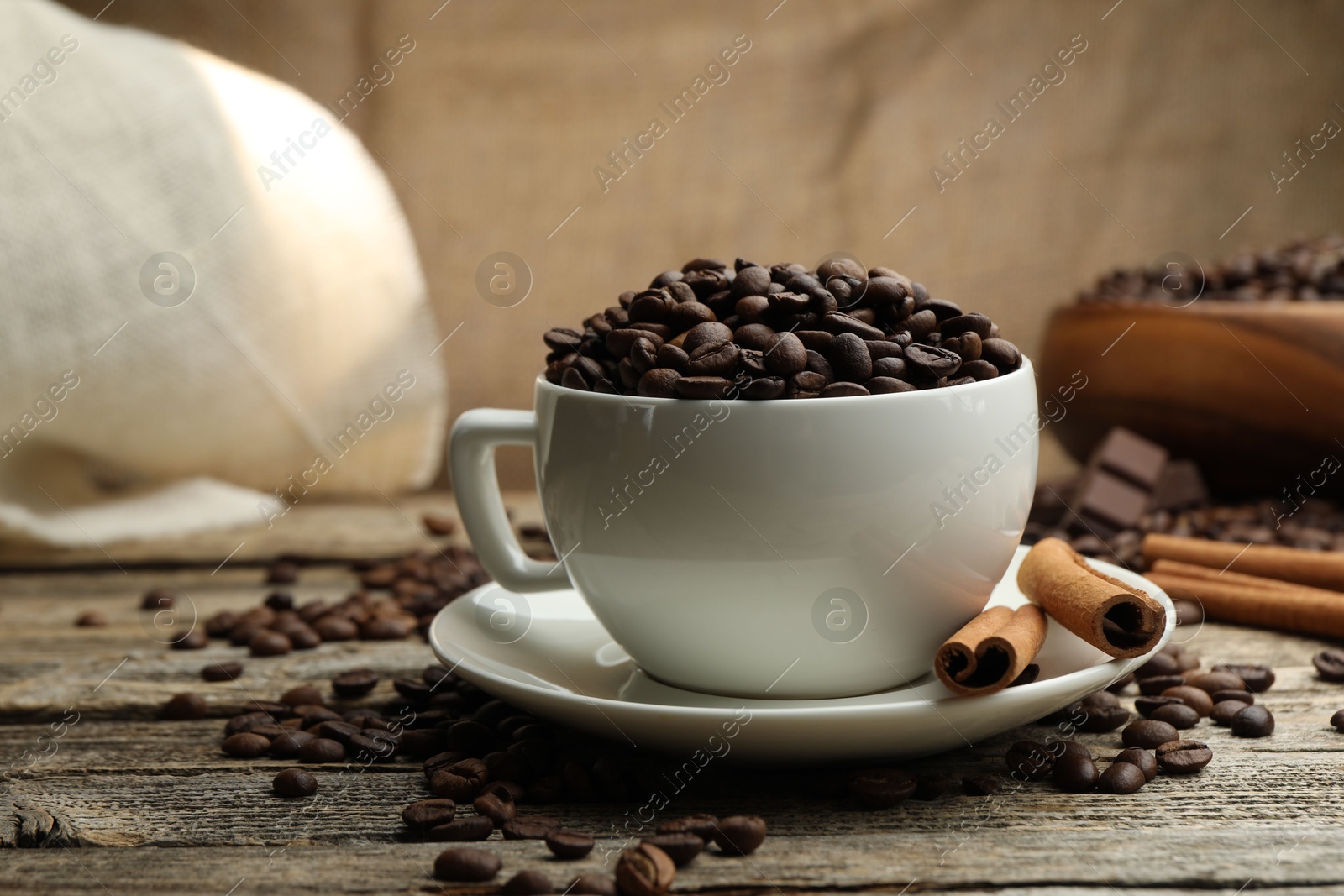 Photo of Aromatic coffee beans in cup and cinnamon on wooden table, closeup