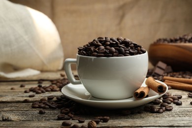 Photo of Aromatic coffee beans in cup and cinnamon on wooden table, closeup