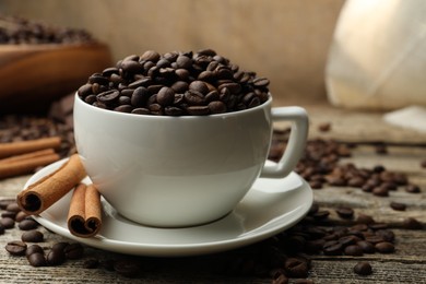 Photo of Aromatic coffee beans in cup and cinnamon on wooden table, closeup