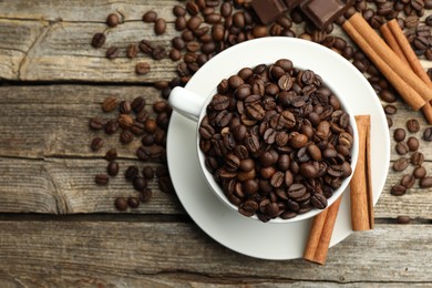 Photo of Aromatic coffee beans in cup, cinnamon and pieces of chocolate on wooden table, flat lay. Space for text