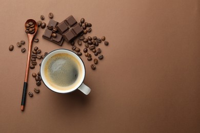 Photo of Aromatic coffee in cup, beans and pieces of chocolate on brown background, flat lay. Space for text