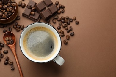 Photo of Aromatic coffee in cup, beans and pieces of chocolate on brown background, flat lay. Space for text