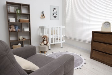 Photo of Baby's room with crib and armchair. Interior design