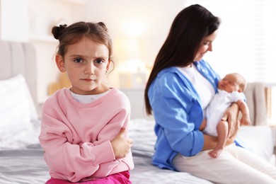 Photo of Jealous little girl upset about mom spending time with newborn baby at home, selective focus