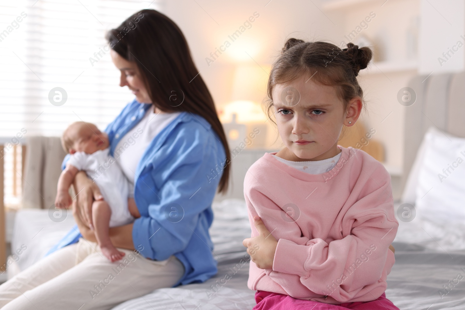 Jealous little girl upset about mom spending time with newborn baby at home, selective focus Photo of Jealous little girl upset about mom spending time with newborn baby at home, selective focus