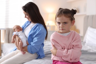 Photo of Jealous little girl upset about mom spending time with newborn baby at home, selective focus