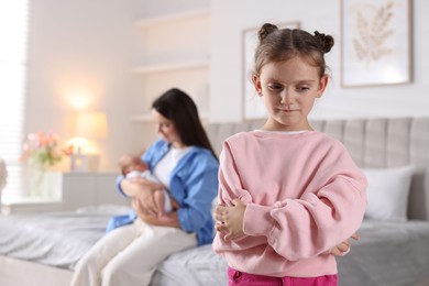 Photo of Jealous little girl upset about mom spending time with newborn baby at home, selective focus