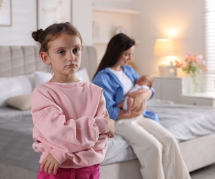 Photo of Jealous little girl upset about mom spending time with newborn baby at home, selective focus