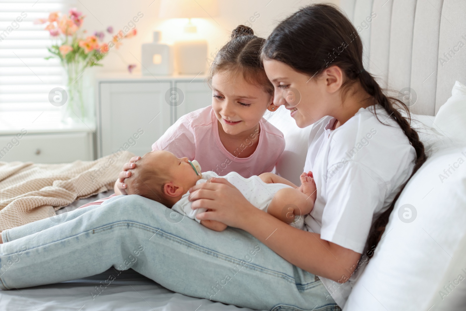Big sisters with newborn baby on bed at home Photo of Big sisters with newborn baby on bed at home