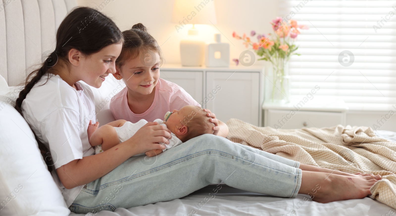 Big sisters with newborn baby on bed at home Photo of Big sisters with newborn baby on bed at home