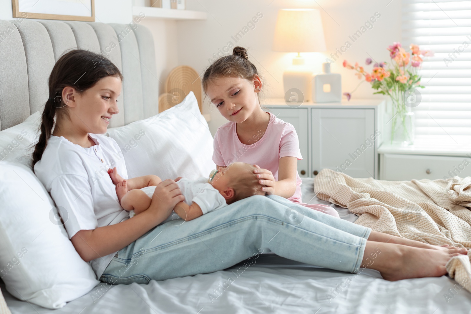 Big sisters with newborn baby on bed at home Photo of Big sisters with newborn baby on bed at home